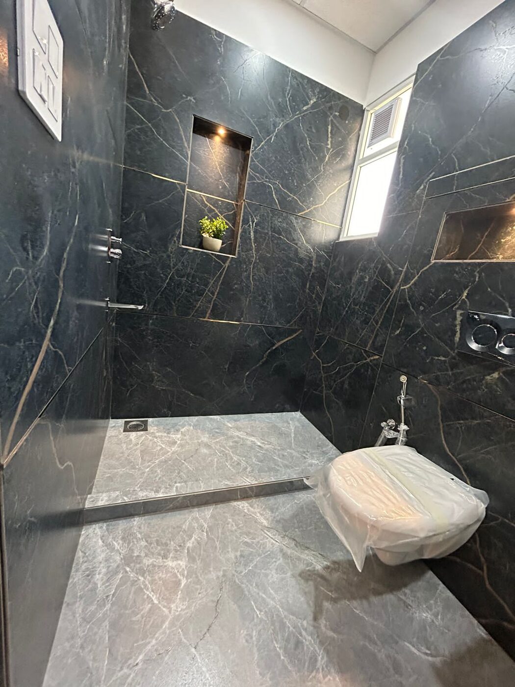 Walk-in shower area in dark tile with a wall-hung WC and a lit niche — Absolute Residency, Sector 92 Mohali