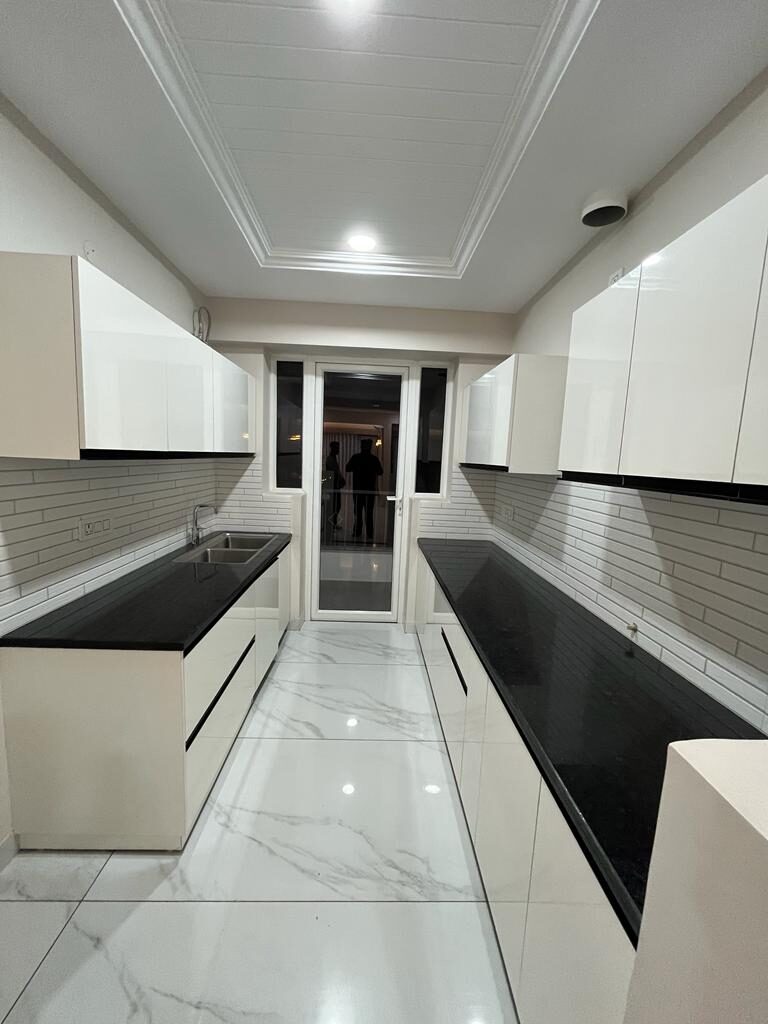 Galley kitchen with white handleless units, granite counters and a service door — Absolute Residency, Sector 92 Mohali