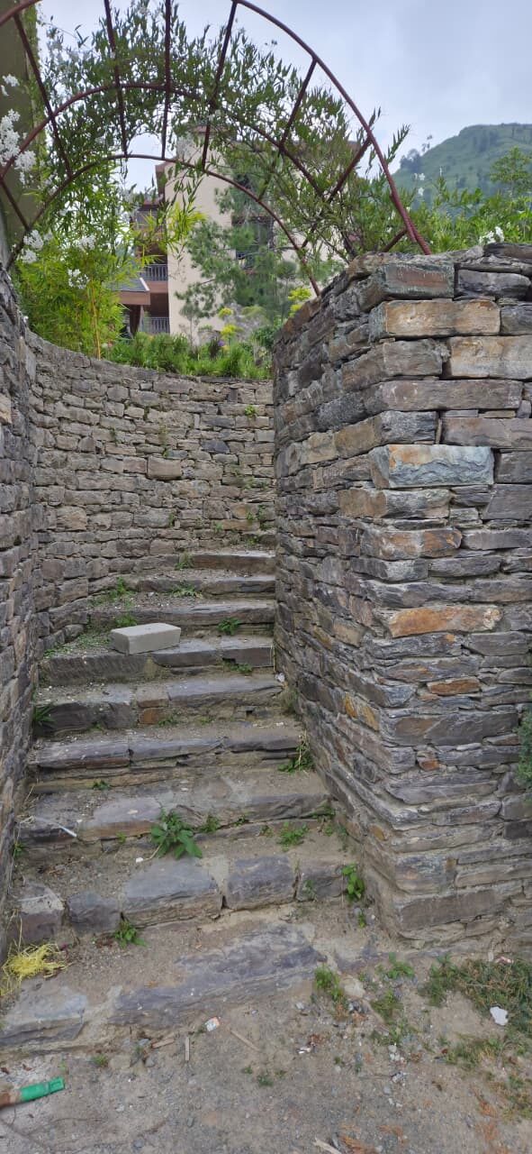 Stone steps rising between dry-stone walls under a metal arch — Himachal Pradesh